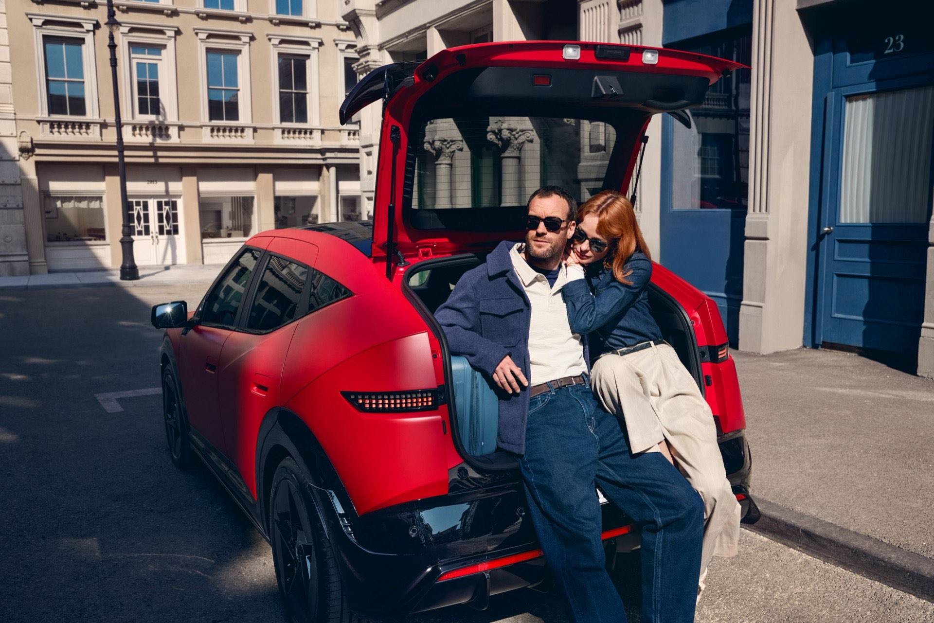 A Hyundai IONIQ 3 egy piros példánya városi utcán, felnyitott csomagtérajtóval, a csomagtartóban táskákkal.