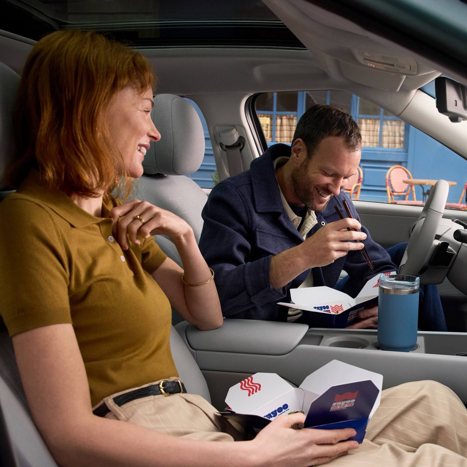 A man and a woman eating take out food in the front seats of the Hyundai IONIQ 3.