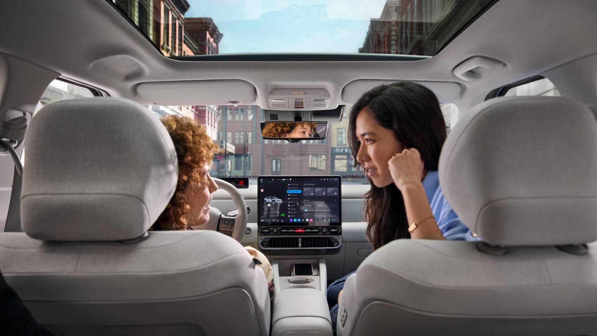 Two woman relaxing and talking in the front seats of the Hyundai IONIQ 3 with the sun roof visible.