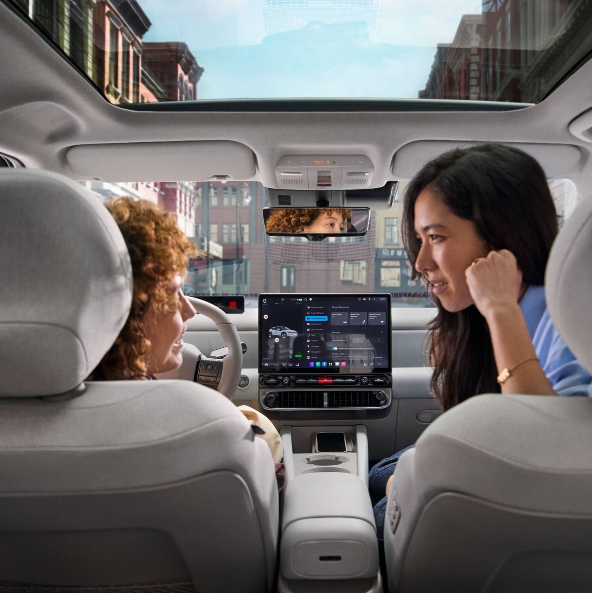 Two woman relaxing and talking in the front seats of the Hyundai IONIQ 3 with the sun roof visible.