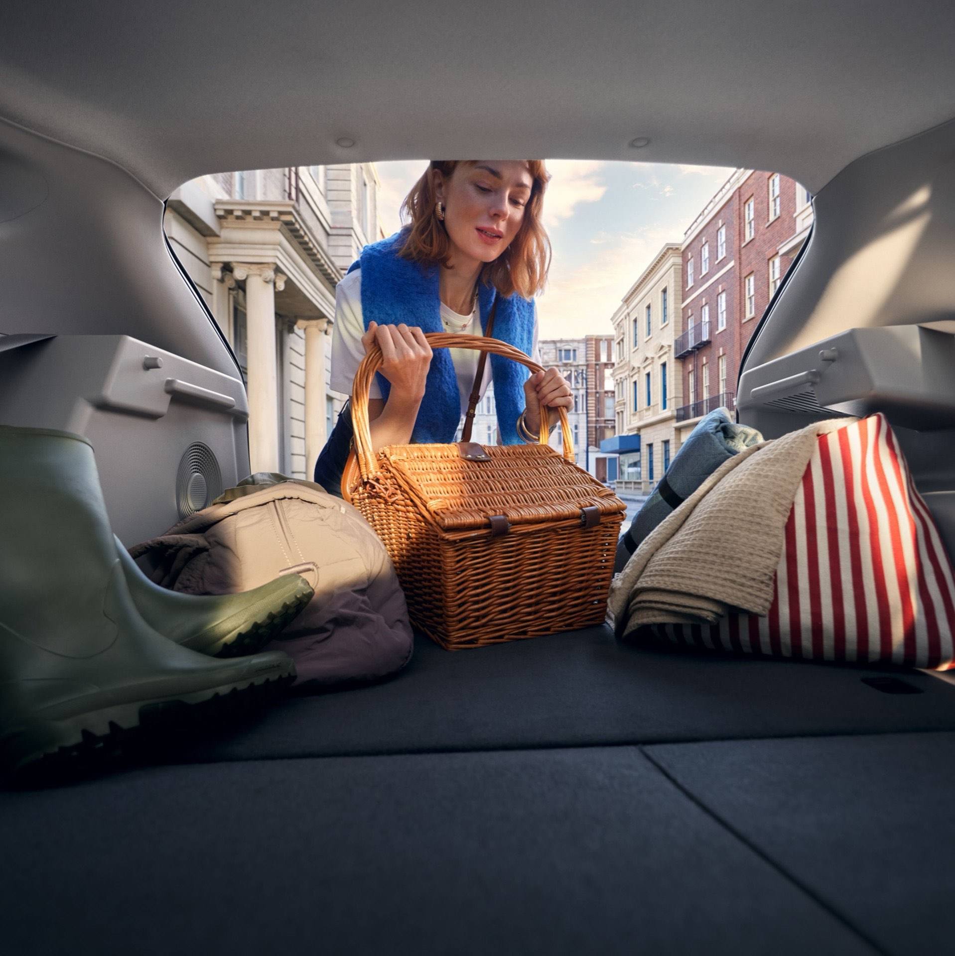 A woman loading a picnic basket into the hatchback of the Hyundai IONIQ 3, rear seats folded down.