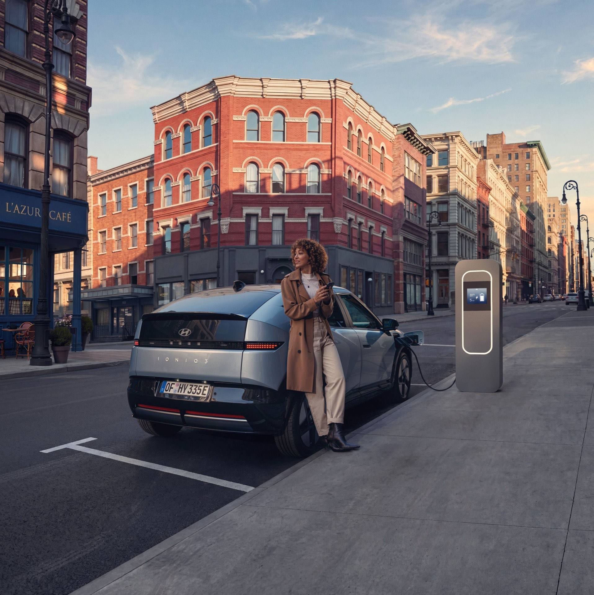 Hyundai IONIQ 3 charging on a city street with a woman leaning on the rear bumper.