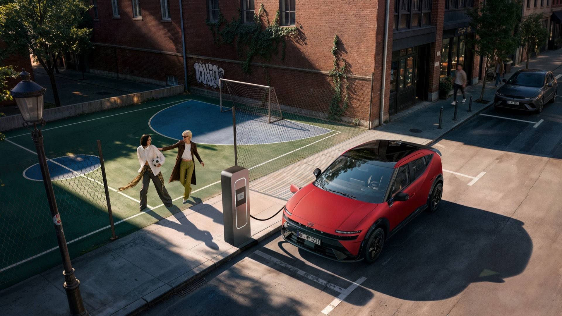 Hyundai IONIQ 3 charging on a city street with two people playing football next to it.