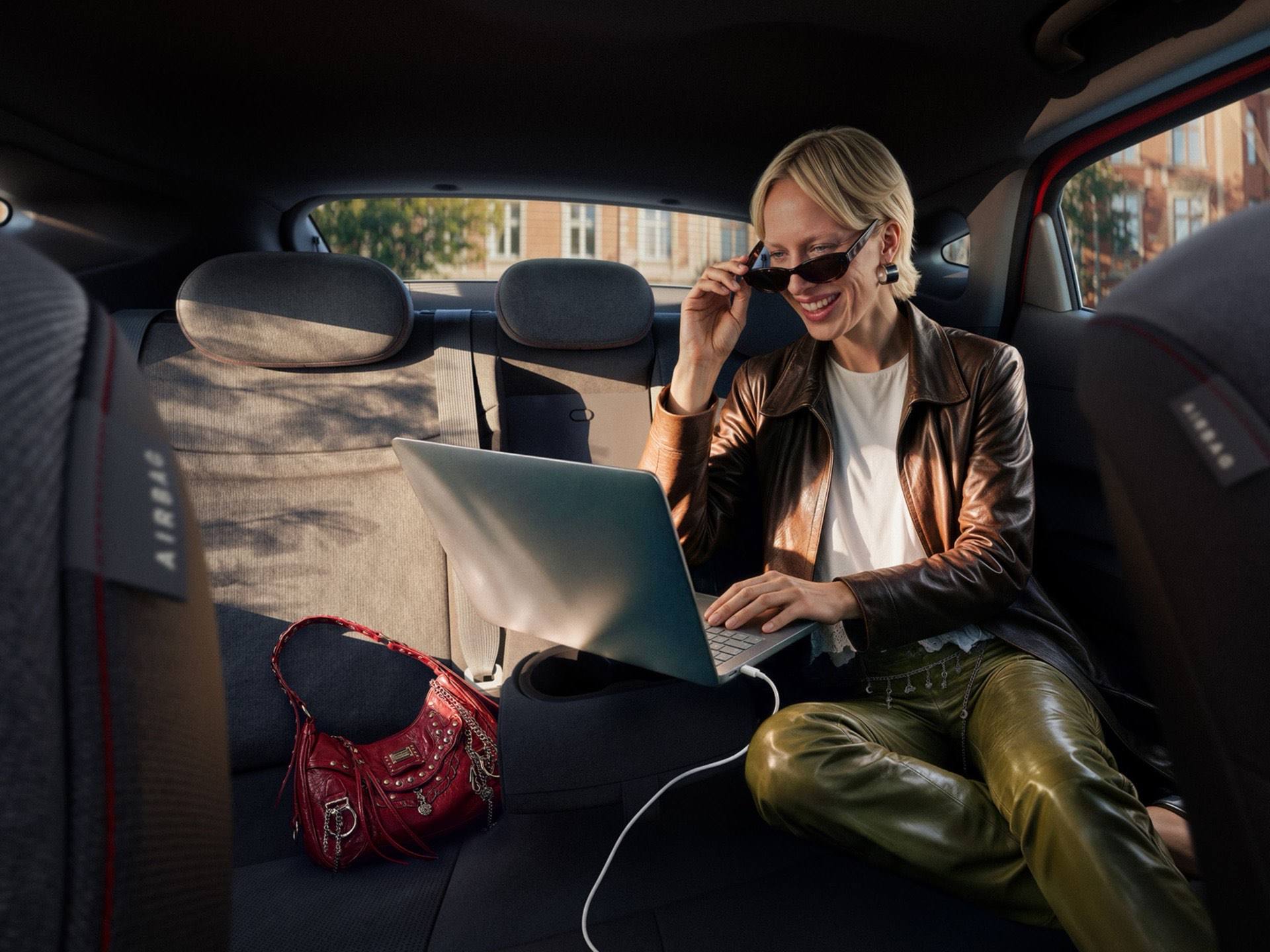 A woman typing on a plugged in laptop on the folded down middle rear seat inside the IONIQ 3.