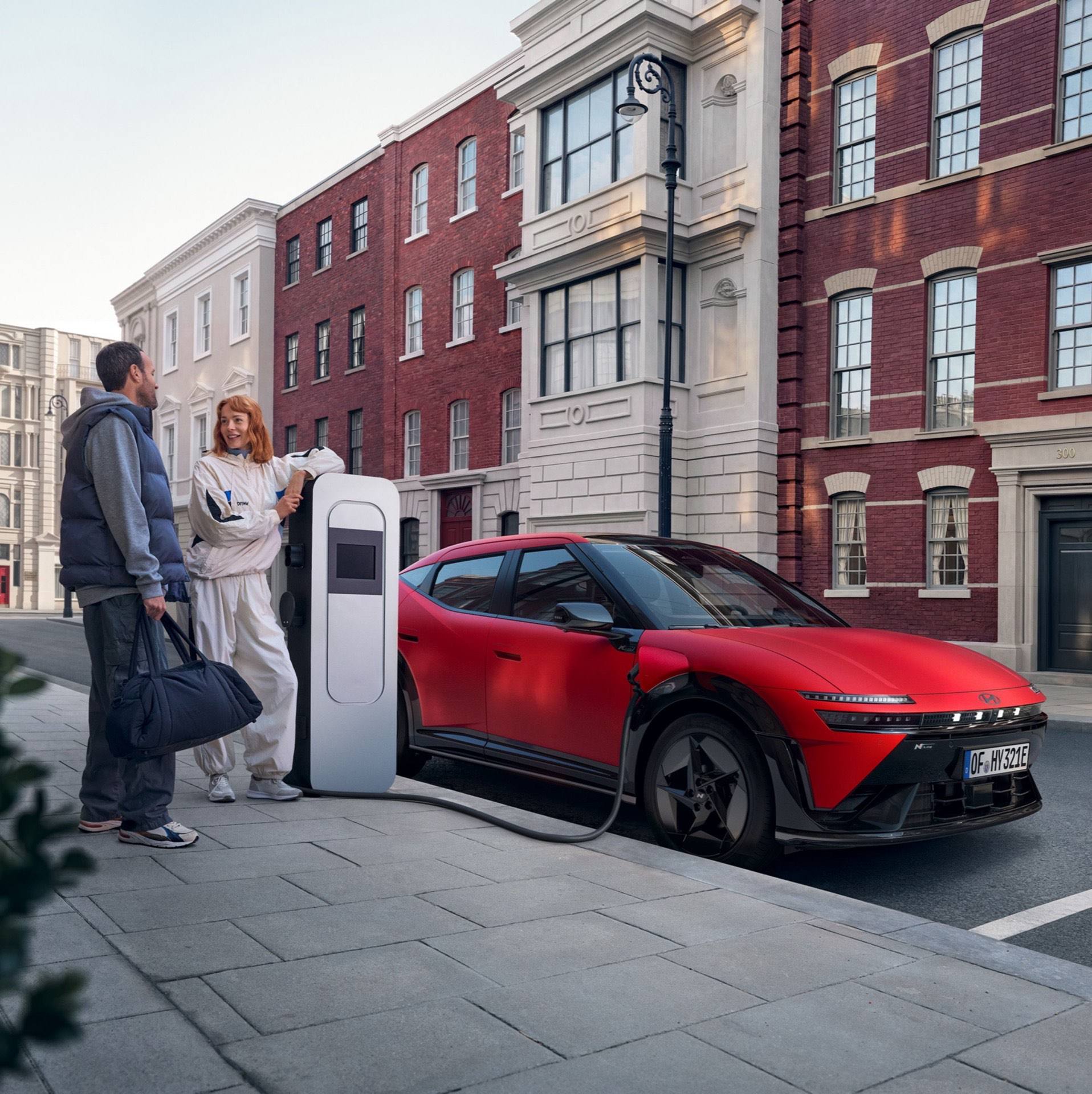 Hyundai IONIQ 3 városi utcán tölt, két ember áll a közelében.